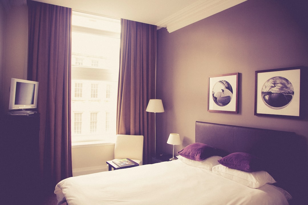 white bed comforter near table lamp, hotel bedroom windows