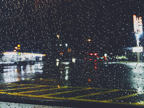 Rain-soaked street outside a glowing café window with blurred neon signs reflecting on wet pavement.