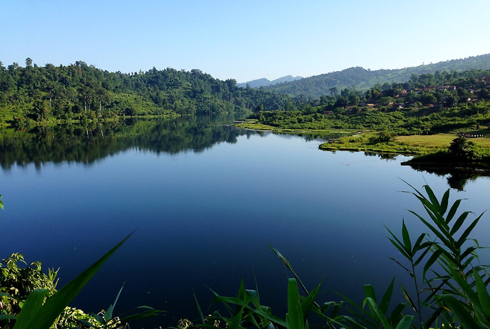 calm body of water near green trees and mountain at daytime