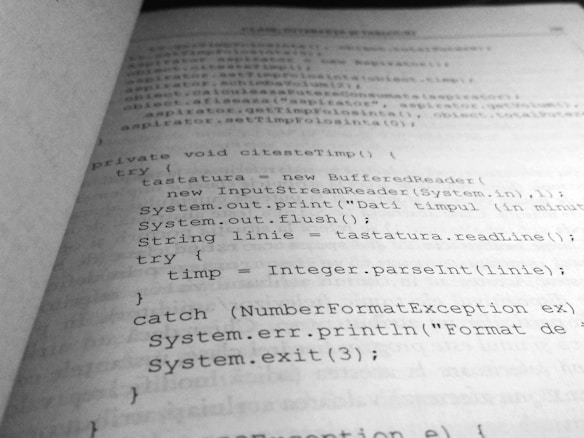 A close-up view of a book page displaying structured code written in a programming language, likely Java. The text is oriented diagonally, capturing sections of code including a method definition and exception handling.