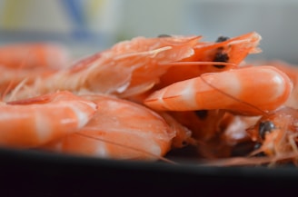 A close-up view of several cooked prawns, showcasing their vibrant orange shells and detailed textures. The image captures the prawns arranged haphazardly, with focus on one prawn at the center.