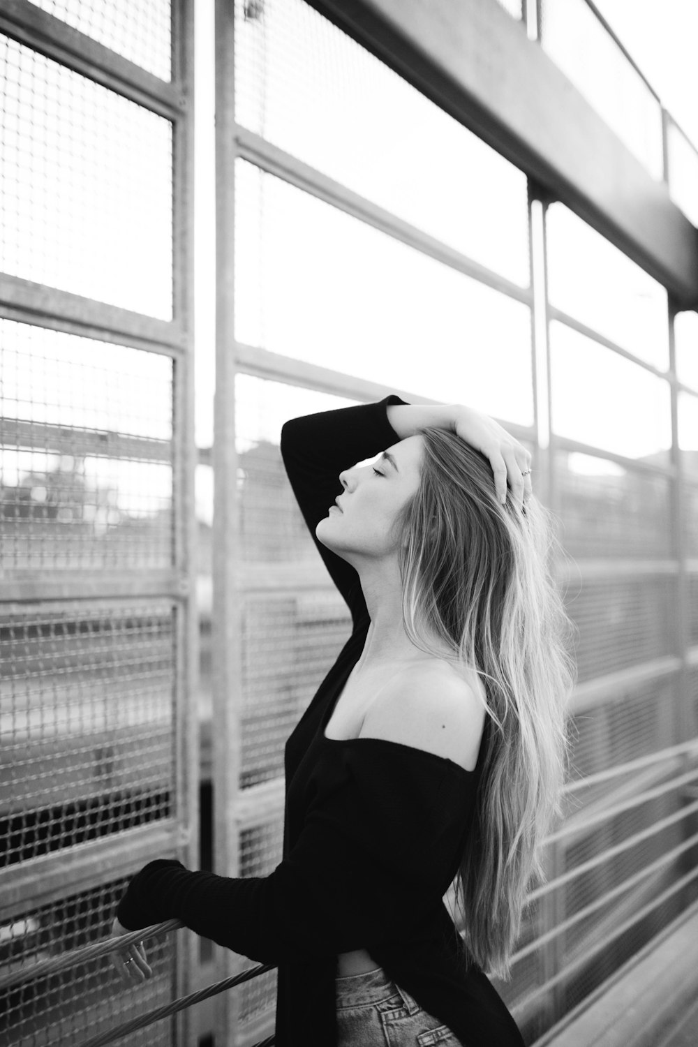 woman wearing off-shoulder top posing beside steel gate in grayscale photography