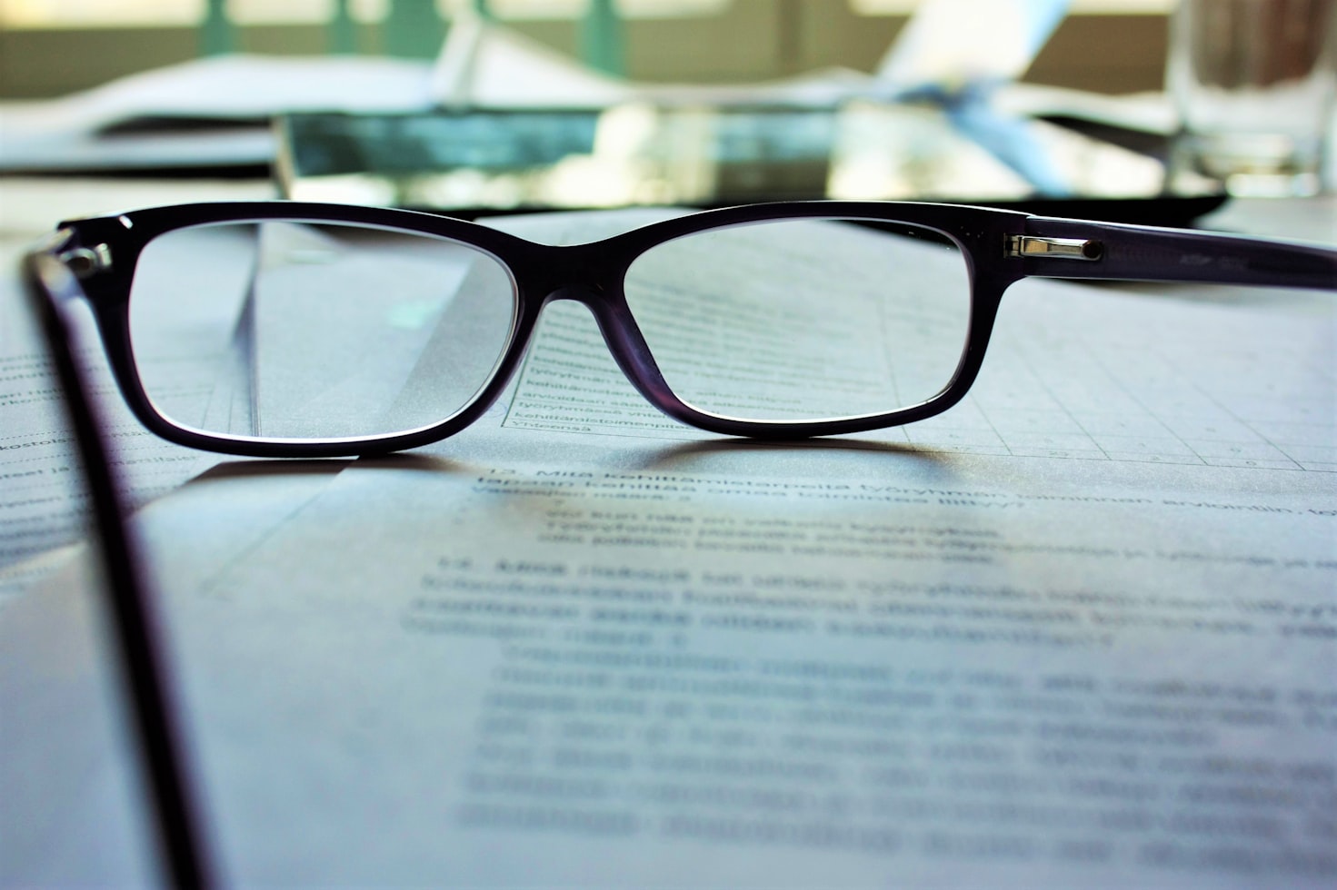 Close-up shot of a pair of black glasses sitting on top of documents. Make sure to read contracts carefully before agreeing to global work and travel opportunities.