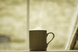 A close-up of a steaming mug filled with coffee, sunlight casting gentle shadows on a soft pastel background.