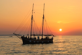 black and white sailboat in body of water during sunset