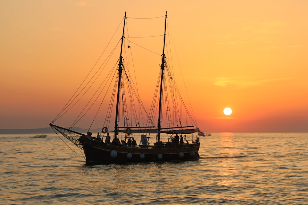 black and white sailboat in body of water during sunset