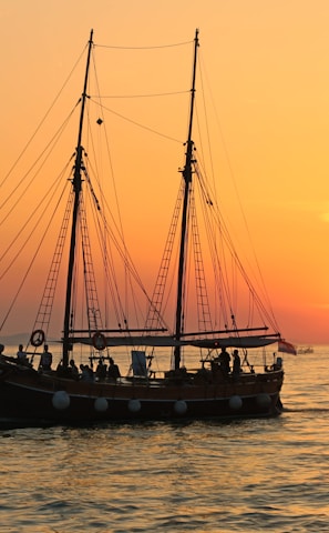 black and white sailboat in body of water during sunset