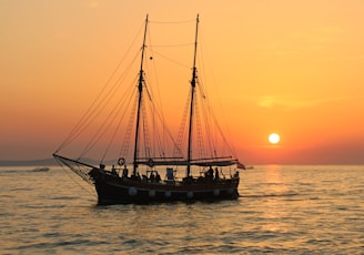 black and white sailboat in body of water during sunset