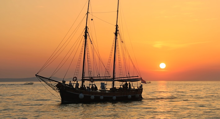 black and white sailboat in body of water during sunset