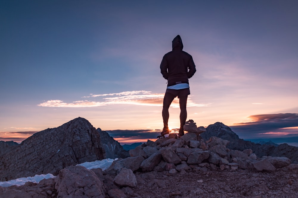Silhouette einer Person, die auf Felsen steht und den Sonnenuntergang beobachtet