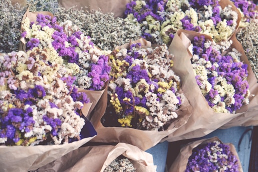 Several bouquets of dried flowers wrapped in brown paper, featuring a mix of purple, white, and yellow hues. The flowers are arranged closely together, creating a vibrant display.