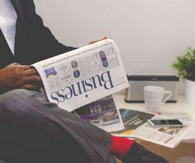 person sitting near table holding a business section of a newspaper