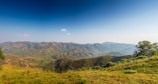 Rolling hills covered in grass and scattered trees extend into the distance under a clear blue sky. The landscape features gentle inclines and valleys with varying shades of green and brown.
