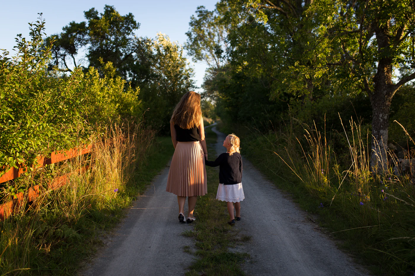 A woman and a child walking away down a country lane in evening light