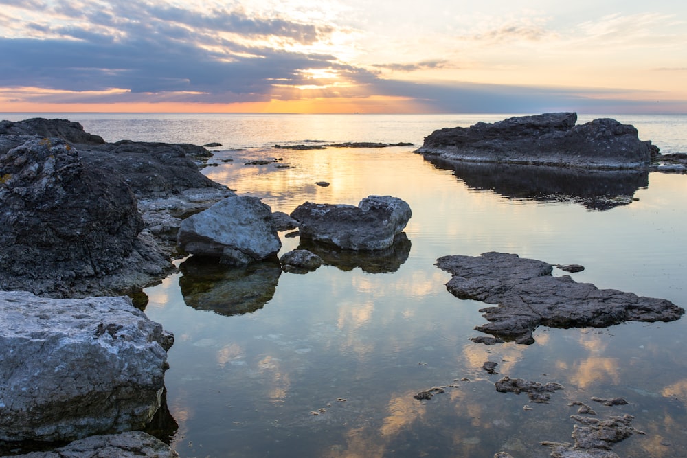 rocks on body of water under cloudy sky