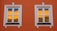 Two white-framed windows are set in an orange wall. The glass reflects a warm yellow hue with a hint of blue sky, possibly showing part of another building or structure. The window frames are detailed with decorative white moldings.