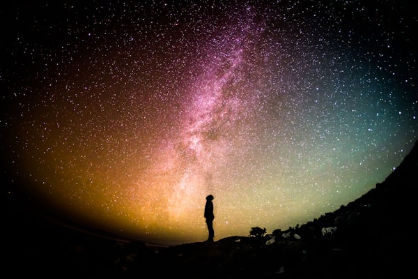 Silhouette of person looking up at colourful night sky with stars and Milky Way