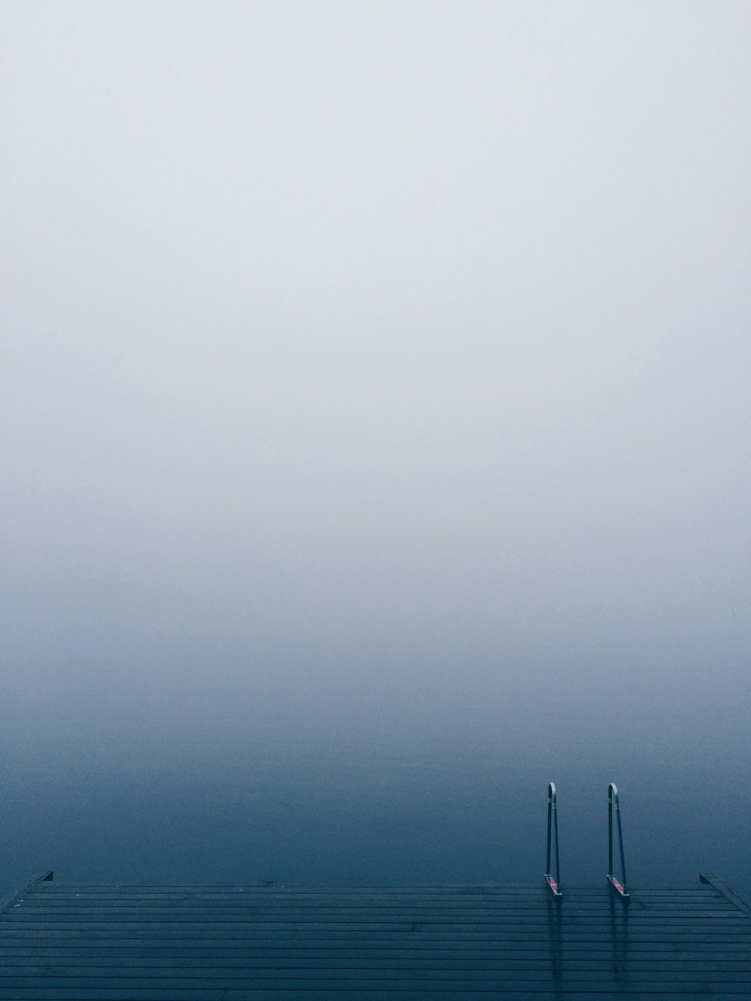 Lake pier with a ladder on serene waters on a foggy day