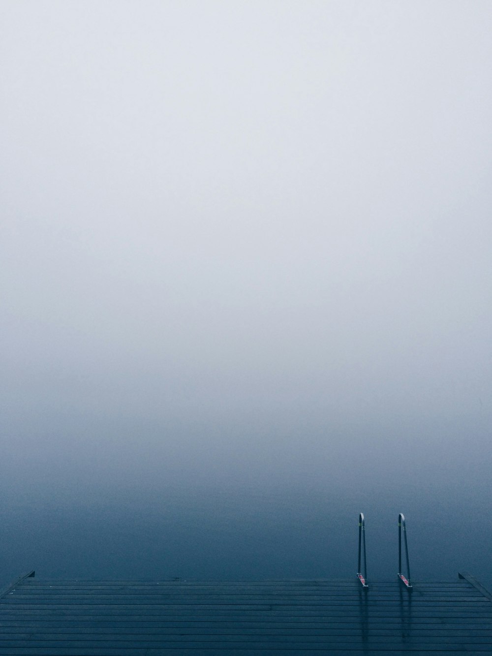 Lake pier with a ladder on serene waters on a foggy day