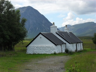 A charming stone cottage nestled among green hills in the Peak District under a bright blue sky.