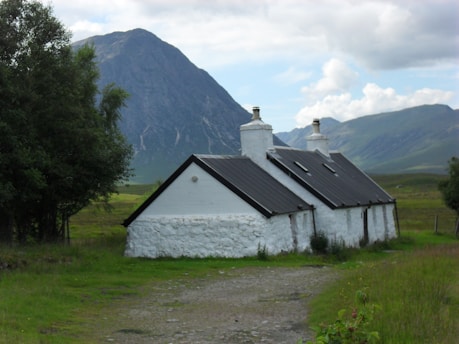 A charming stone cottage nestled among green hills in the Peak District under a bright blue sky.