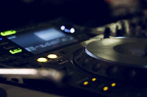 Close-up of DJ equipment with glowing buttons and dark ambient lighting.