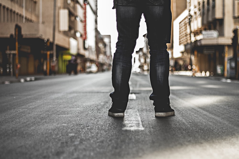 selective focus photography of person standing on blacktop road between buildings