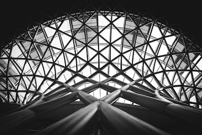 Intricate lattice architecture with a large dome made of geometric patterns. The structure consists of intersecting steel beams forming triangle shapes, leading to a modern and industrial aesthetic.