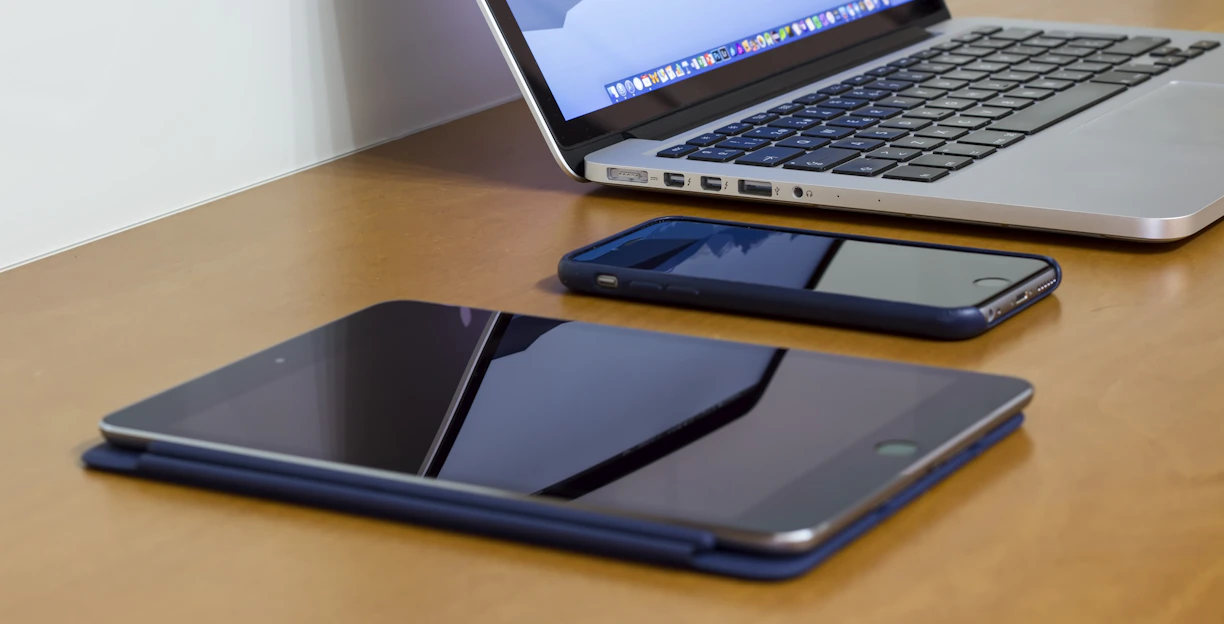 A sleek display of a tablet, laptop, and smartwatch arranged on a wooden desk with soft natural light.