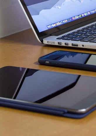 A sleek display of a tablet, laptop, and smartwatch arranged on a wooden desk with soft natural light.