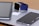 A collection of modern gadgets is arranged on a wooden surface, including a tablet, a smartwatch with a blue band, and a smartphone, all placed on top of a laptop with a visible Apple logo.