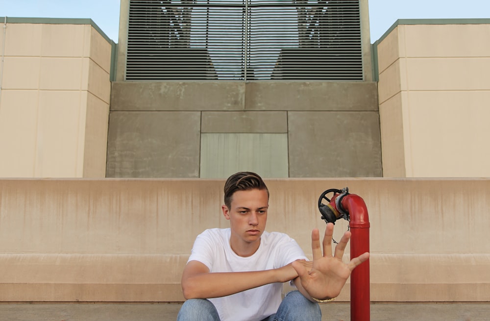 man wearing white t-shirt showing left palm while sitting near building