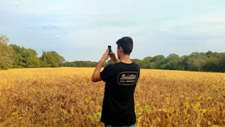A farmer in a lush green field checking crops with a smartphone.