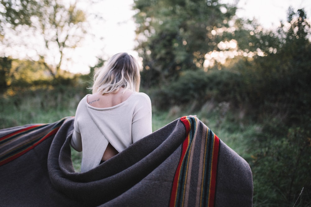 standing woman holding gray blanket surrounded by green grass