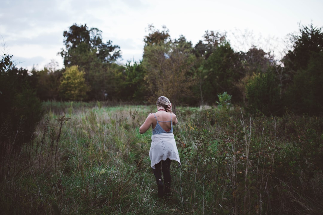 woman walking on green field surrounded with tall and green trees