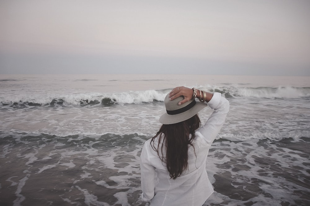 woman holding hat beside body of water