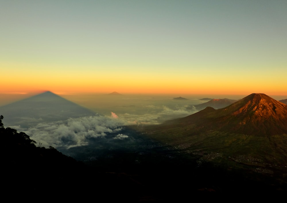 aerial photo of mountain near land covered by white clouds at golden hour