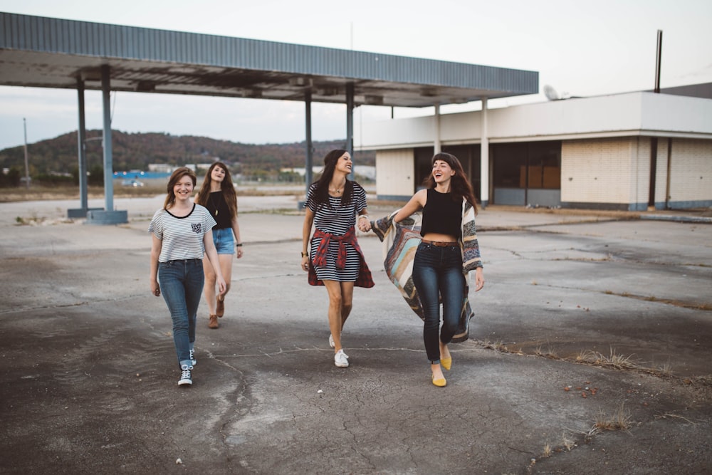 four girls walking near warehouse during daytime