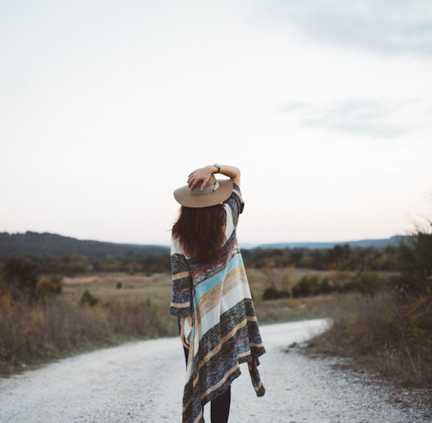 standing woman holding her hat at the middle of the road during day