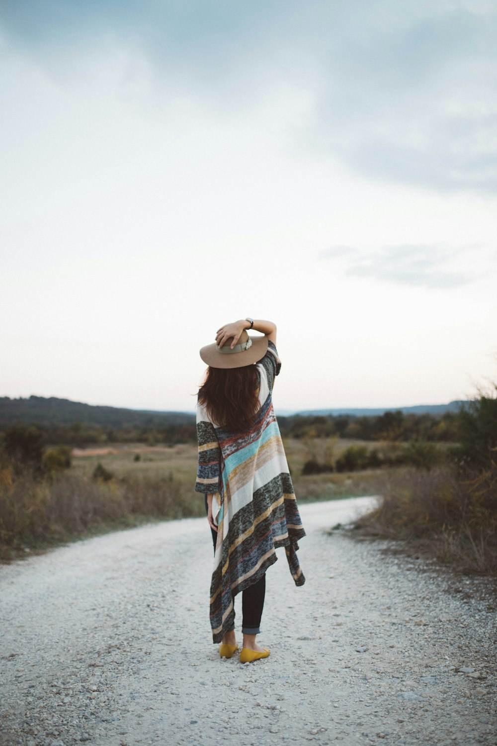 standing woman holding her hat at the middle of the road during day