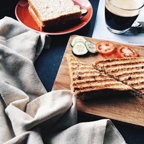 sliced grilled bread beside tomatoes and cucumbers on brown wooden board
