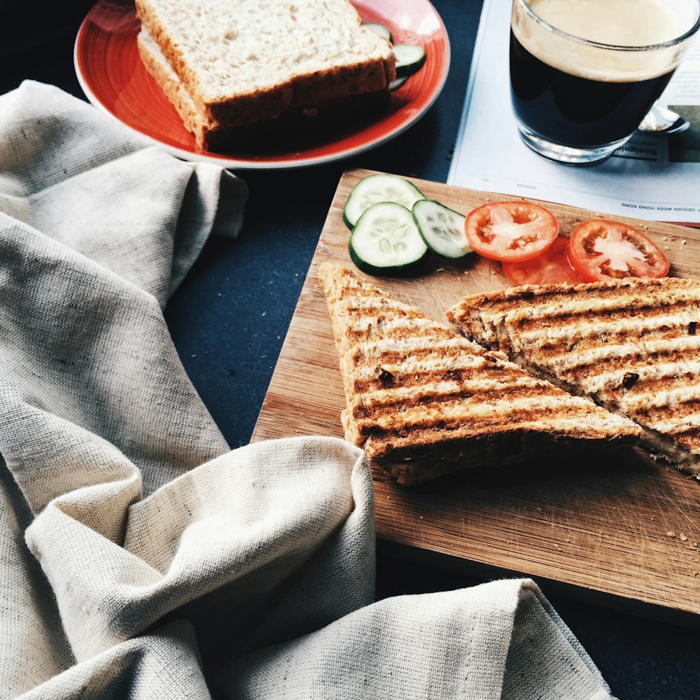 sliced grilled bread beside tomatoes and cucumbers on brown wooden board