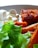 A close-up of a plate containing fresh green lettuce, white cubed cheese, crispy roasted sweet potatoes, and a piece of breaded meat. The textures and colors of the food items are vivid, with light softly illuminating the scene.