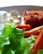 A close-up of a plate containing fresh green lettuce, white cubed cheese, crispy roasted sweet potatoes, and a piece of breaded meat. The textures and colors of the food items are vivid, with light softly illuminating the scene.