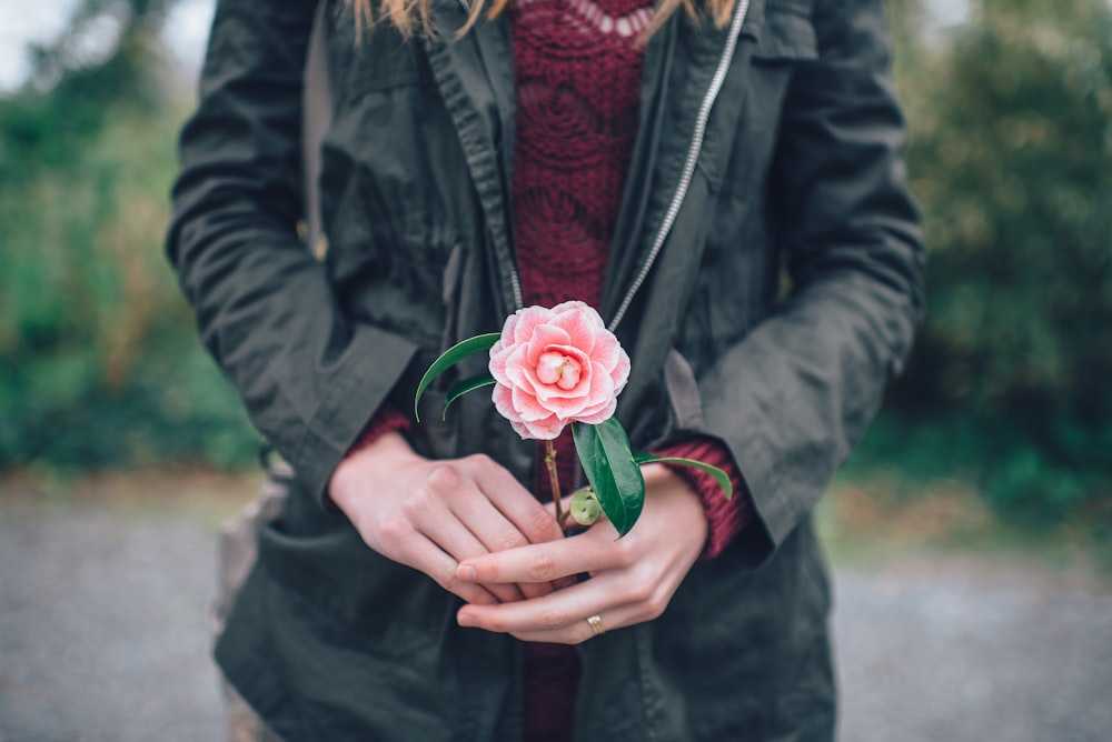 woman holding pink rose standing near trees during daytime