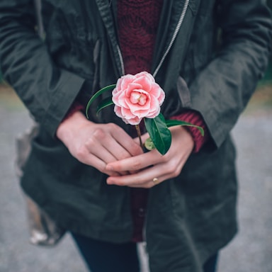 woman in black leather jacket holding pink flower during daytime