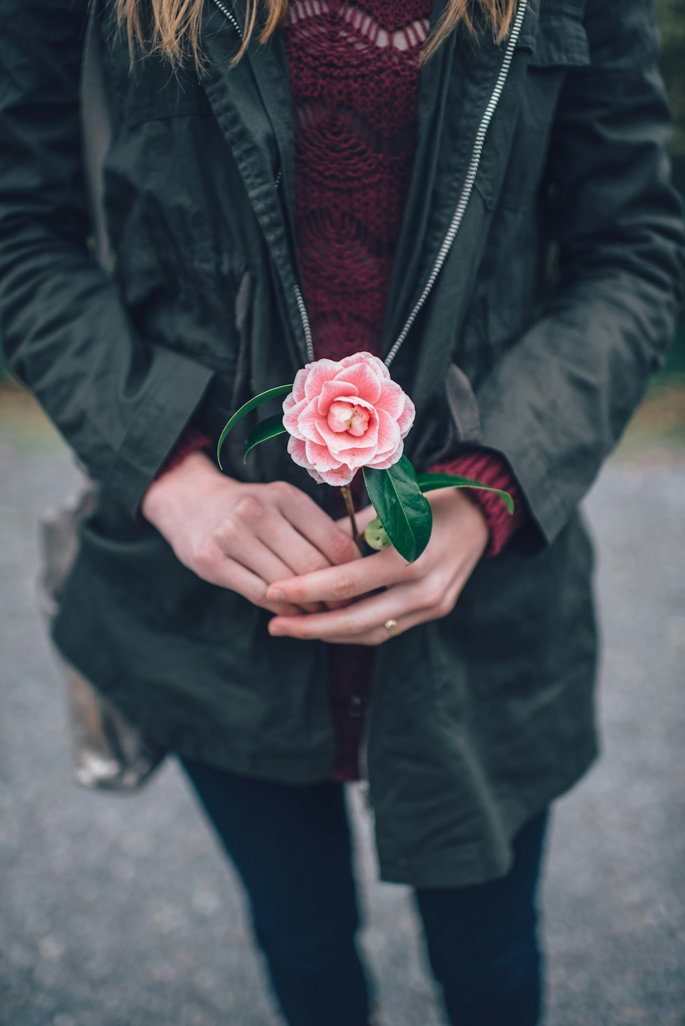 Mujer en chaqueta de cuero negro sosteniendo flor rosa durante el día