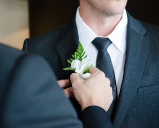 man attaching flower on another man's lapel in a well-lit room