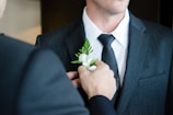 man attaching flower on another man's lapel in a well-lit room