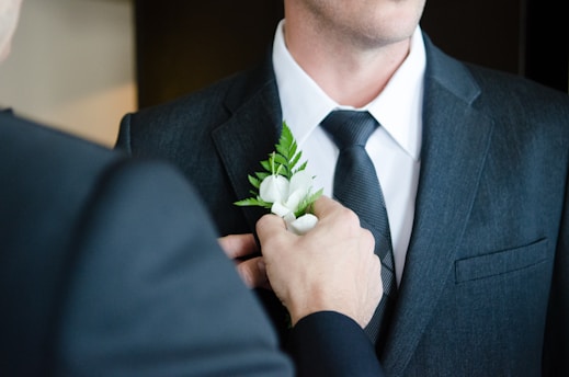 man attaching flower on another man's lapel in a well-lit room